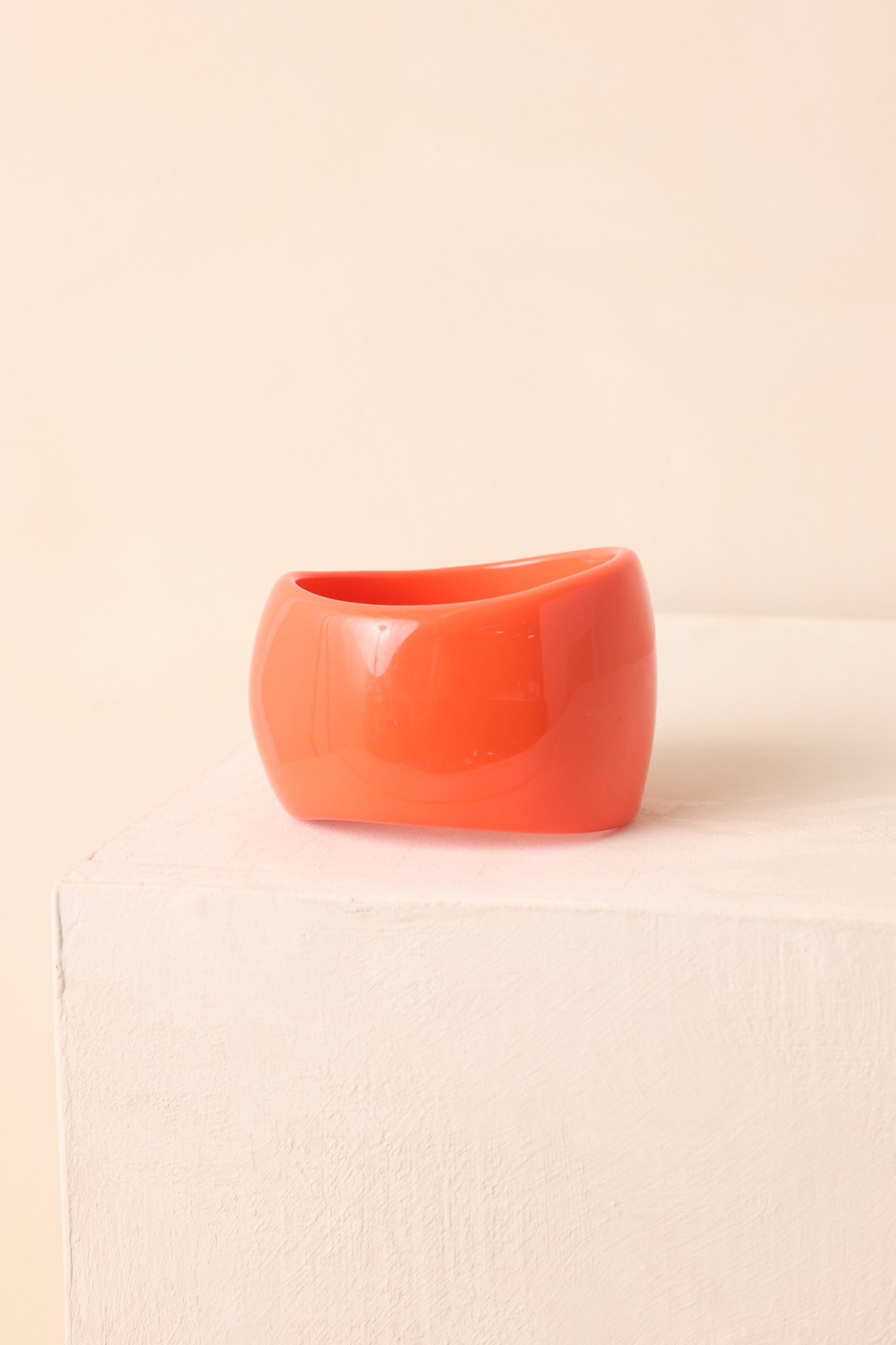 Chunky orange bangle with smooth, high-polish finish shown in a sculptural design.
