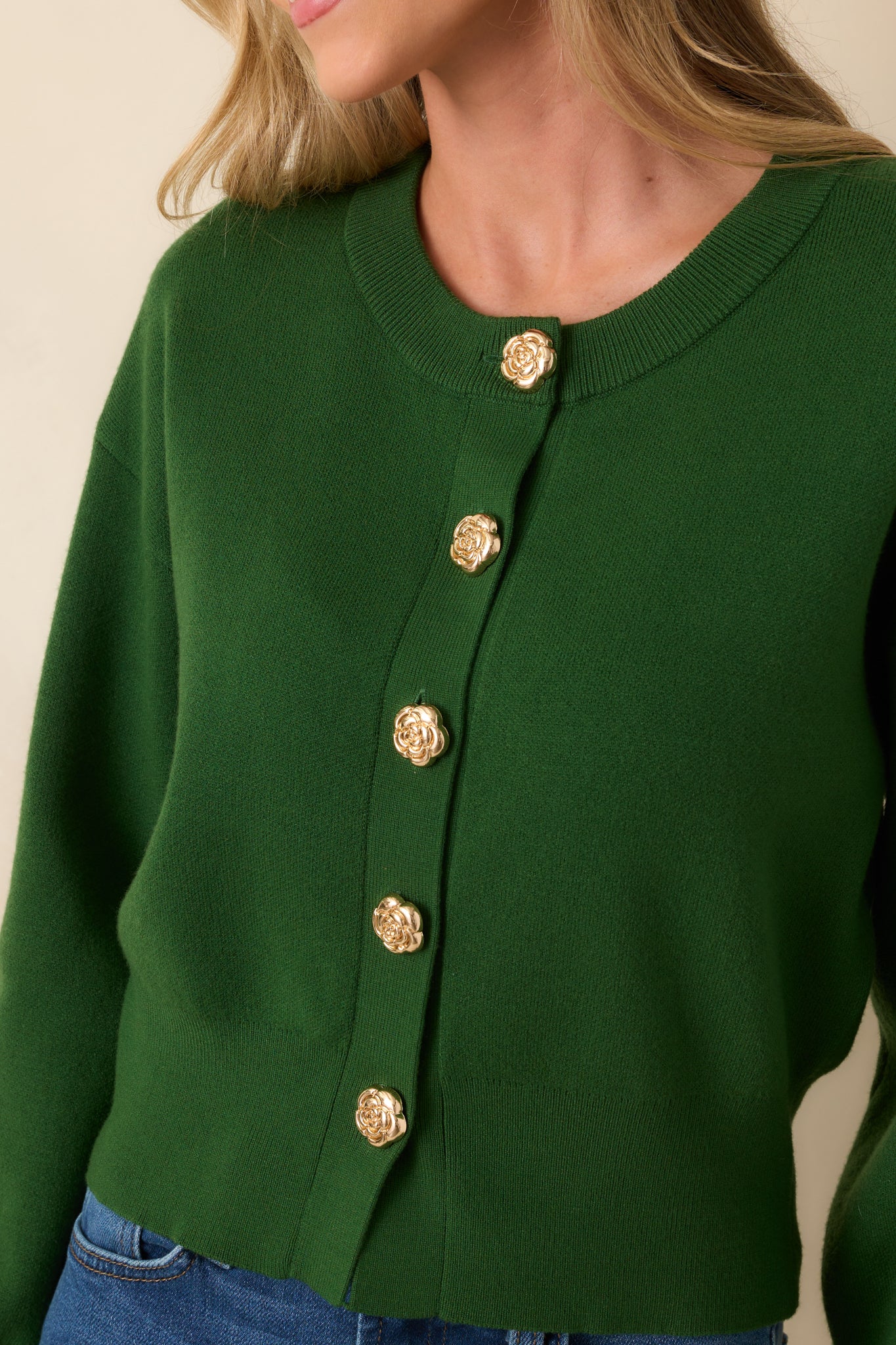 Zoomed-in image of one gold flower-shaped button on the hunter green knit fabric, showing the button’s design and textured ribbing.