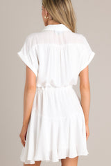 Back view of this white dress features a collared neckline, semi-transparent lace, a half button front, a self-tie waist feature, a lightweight fabric, and folded short sleeves.
