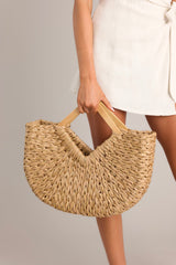Close up view of this tan and gold bag that  features a woven design with gold throughout and a wooden handle.