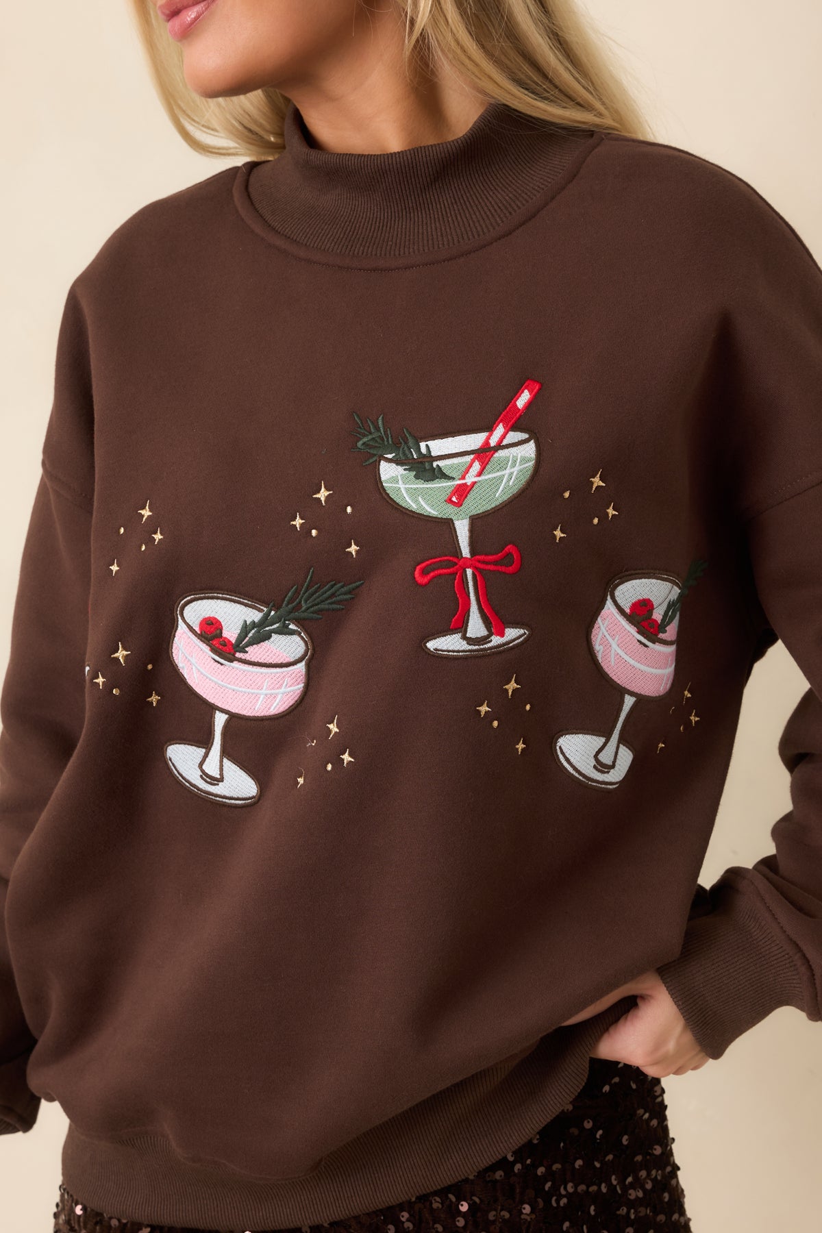 Cocoa brown mock neck sweatshirt featuring three embroidered holiday cocktails, a red bow, and gold star accents.