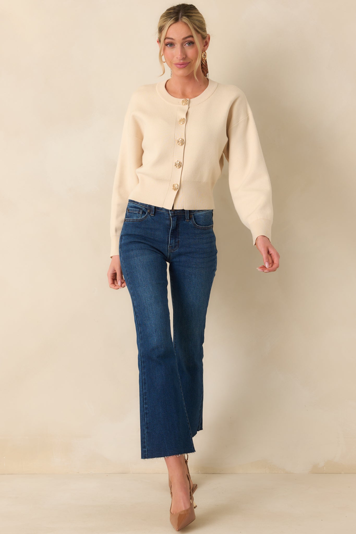 Front view of the beige cardigan worn buttoned up, featuring long sleeves and a crew neckline with a tapered fitted waistband.