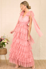 Angled full body view of this pink dress featuring a flattering v-neckline, graceful fabric trailing from the shoulders, a chic self-tie waist belt, and multiple tiers and layers of ethereal tulle for a whimsical touch.