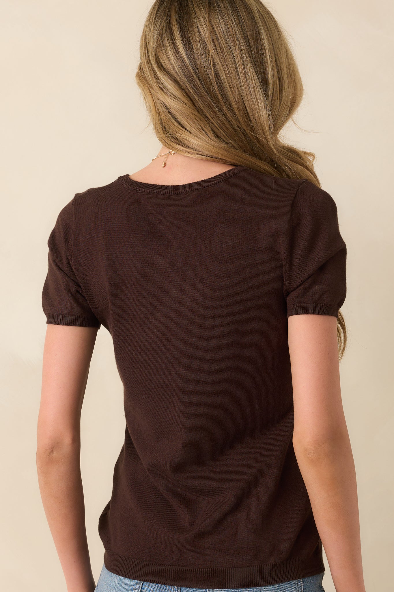 A back view of the dark brown sweater top displaying the short sleeves and consistent ribbed hem finish.