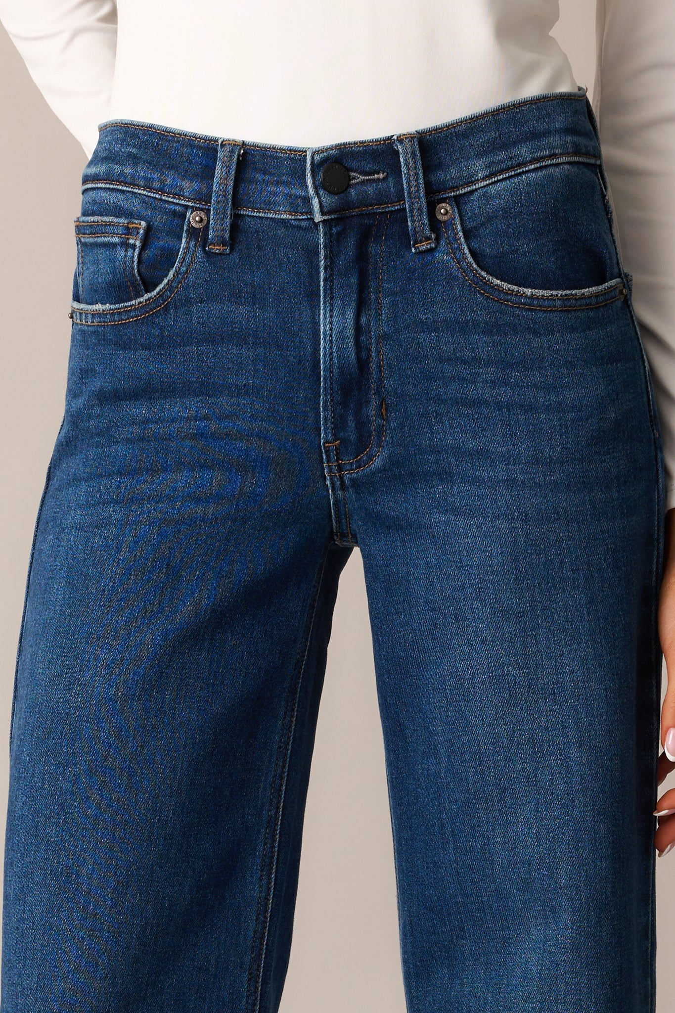 A close-up of the jeans’ button and zipper closure, showcasing the sturdy stitching, belt loops, and high-waisted structure.