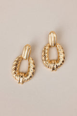 Overhead view of these gold earrings with rectangular-shaped studs, textured dangles, secure post backings.