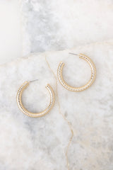 Overhead view of these gold hoop earrings that feature a textured gold finish, and a secure post-back fastening.