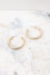 Angled overhead view of these gold hoop earrings that feature a textured gold finish, and a secure post-back fastening.