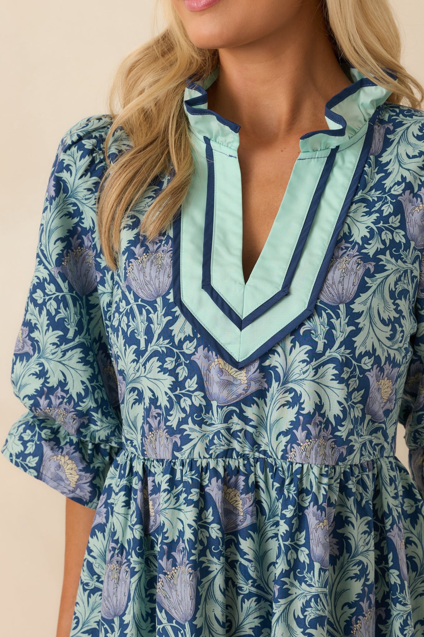 Close-up of the ruffle neckline, floral print, and trim detailing on the navy mini dress.