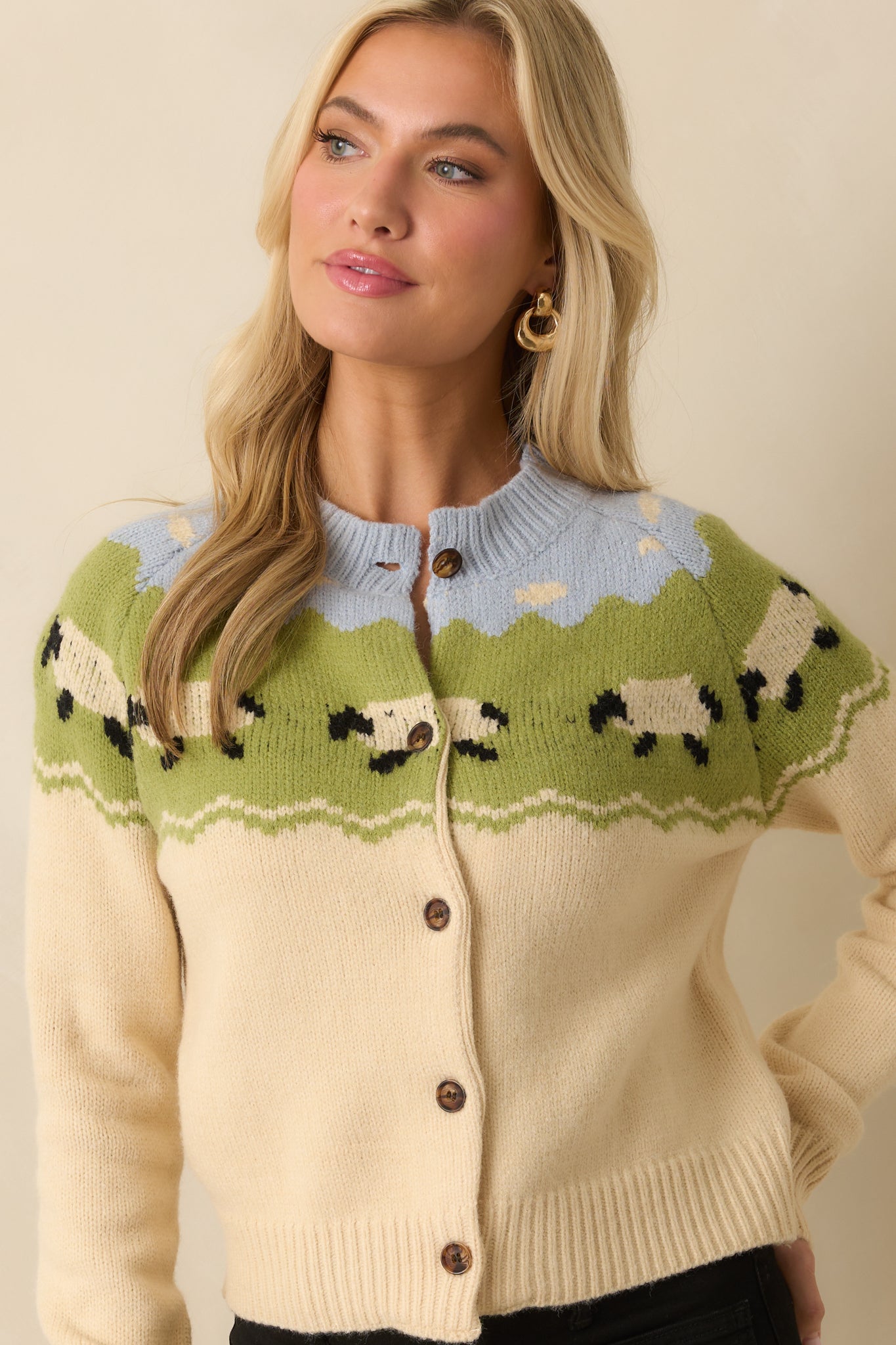 Focused crop of ecru cardigan with visible button-front closure and decorative yoke pattern.