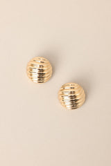 Overhead view of these view of these gold earrings with circular shape, wave-like texture, secure post backing