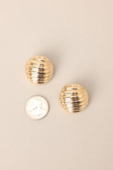 Size comparison of these view of these gold earrings with circular shape, wave-like texture, secure post backing