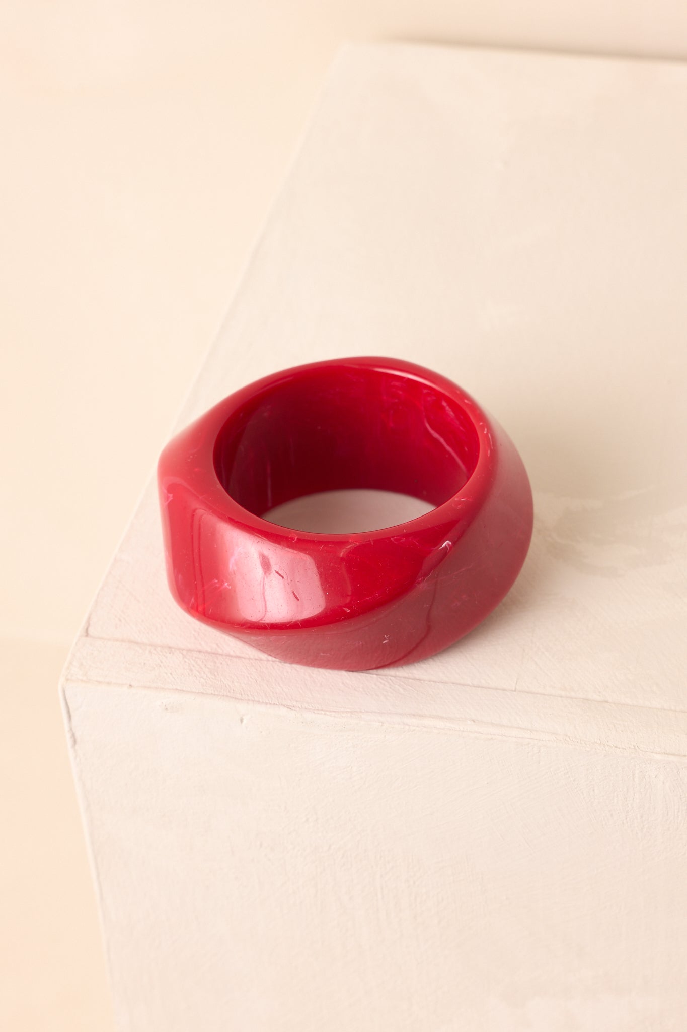 Glossy red marbled bangle displayed on beige background with bold, chunky silhouette.