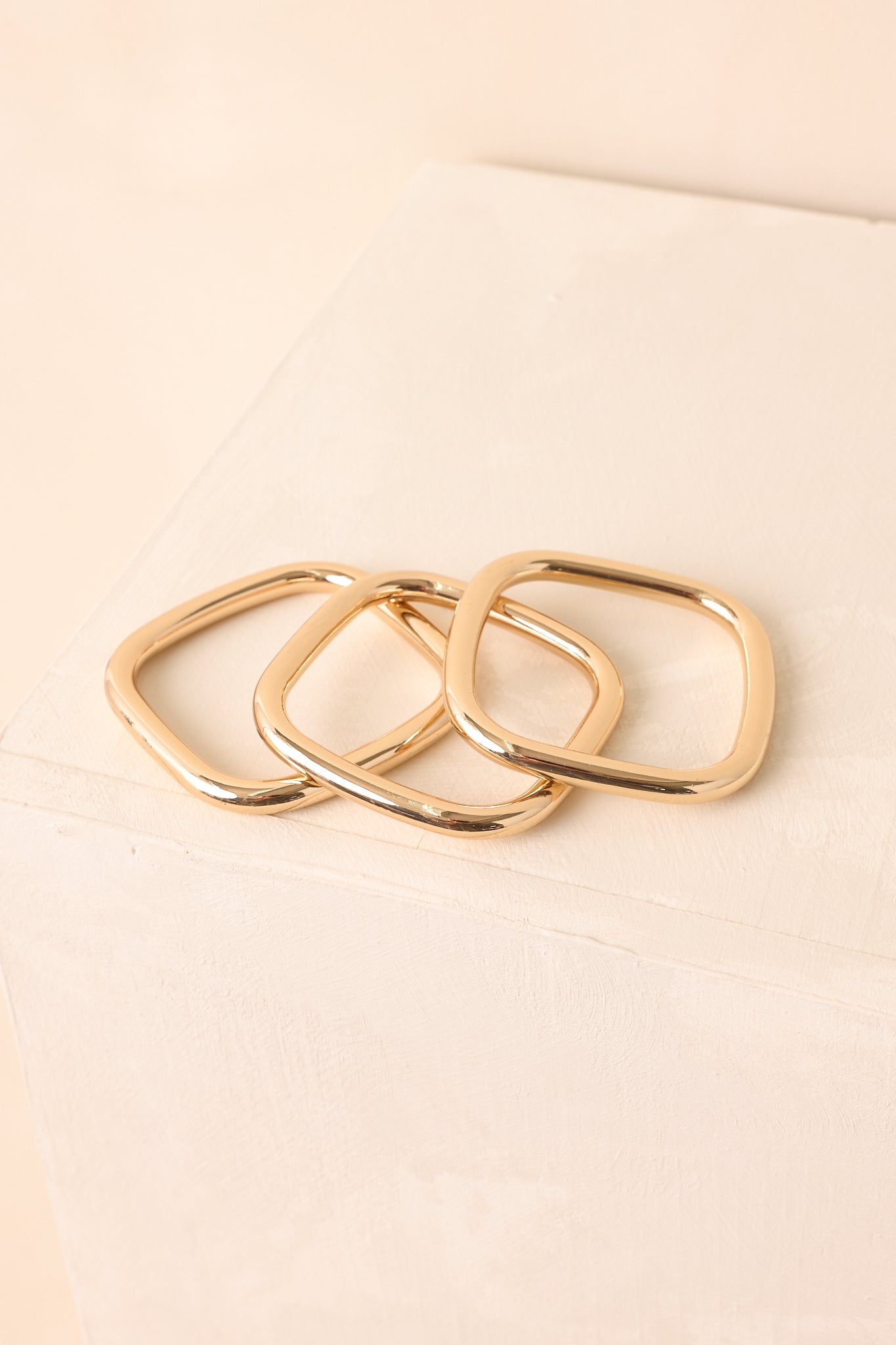 A close-up cropped shot highlighting the polished surface and square silhouette of the gold bangles.