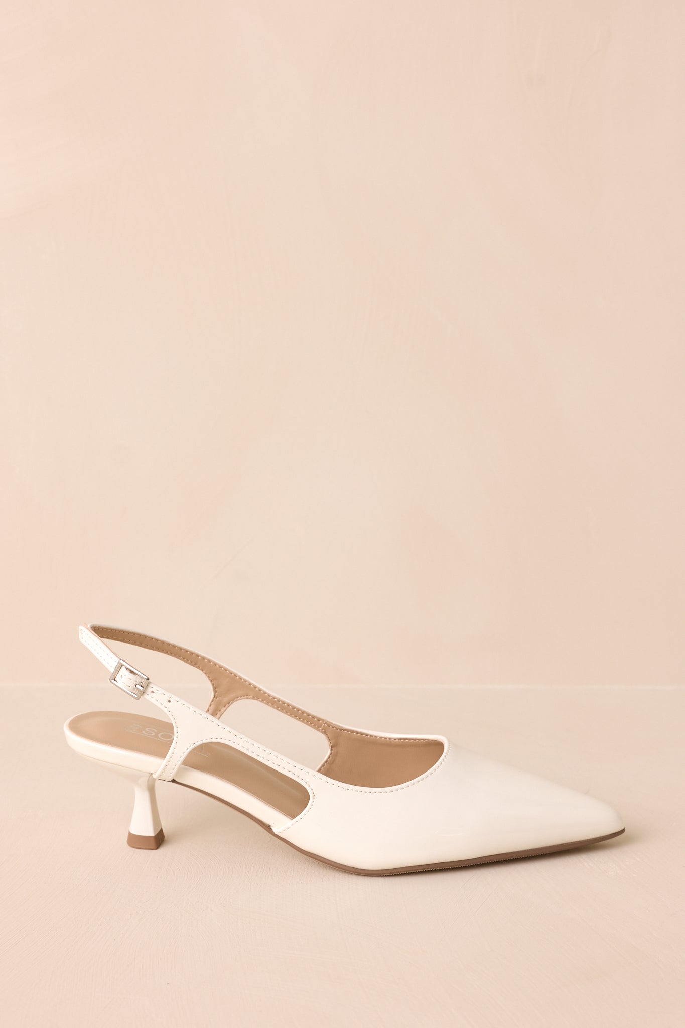 Gold buckle white patent pointed-toe heel with side cutout side view on backdrop.
