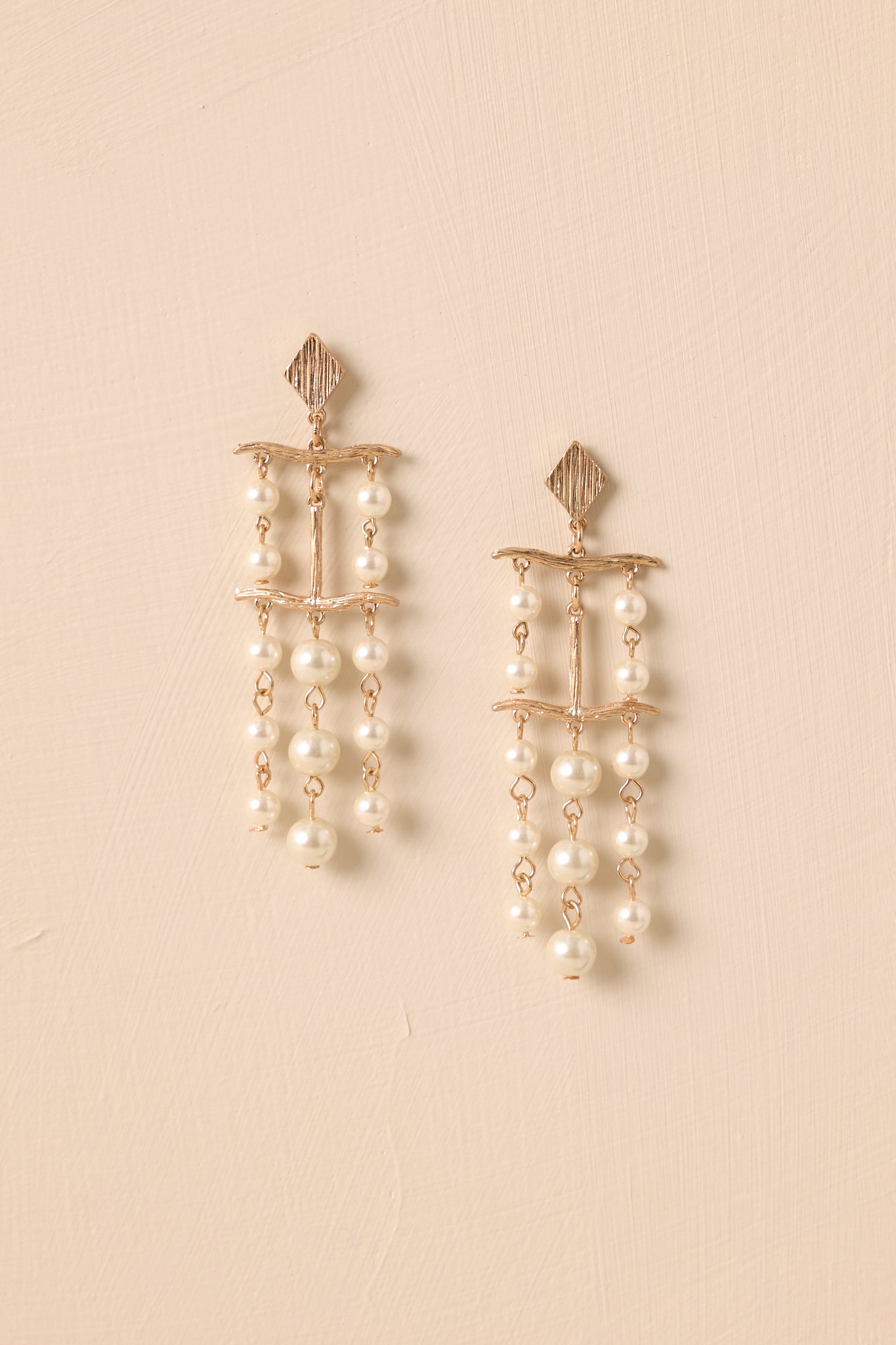 Flat lay of gold chandelier earrings with diamond stud, T-shaped charm, and pearl chain drops.