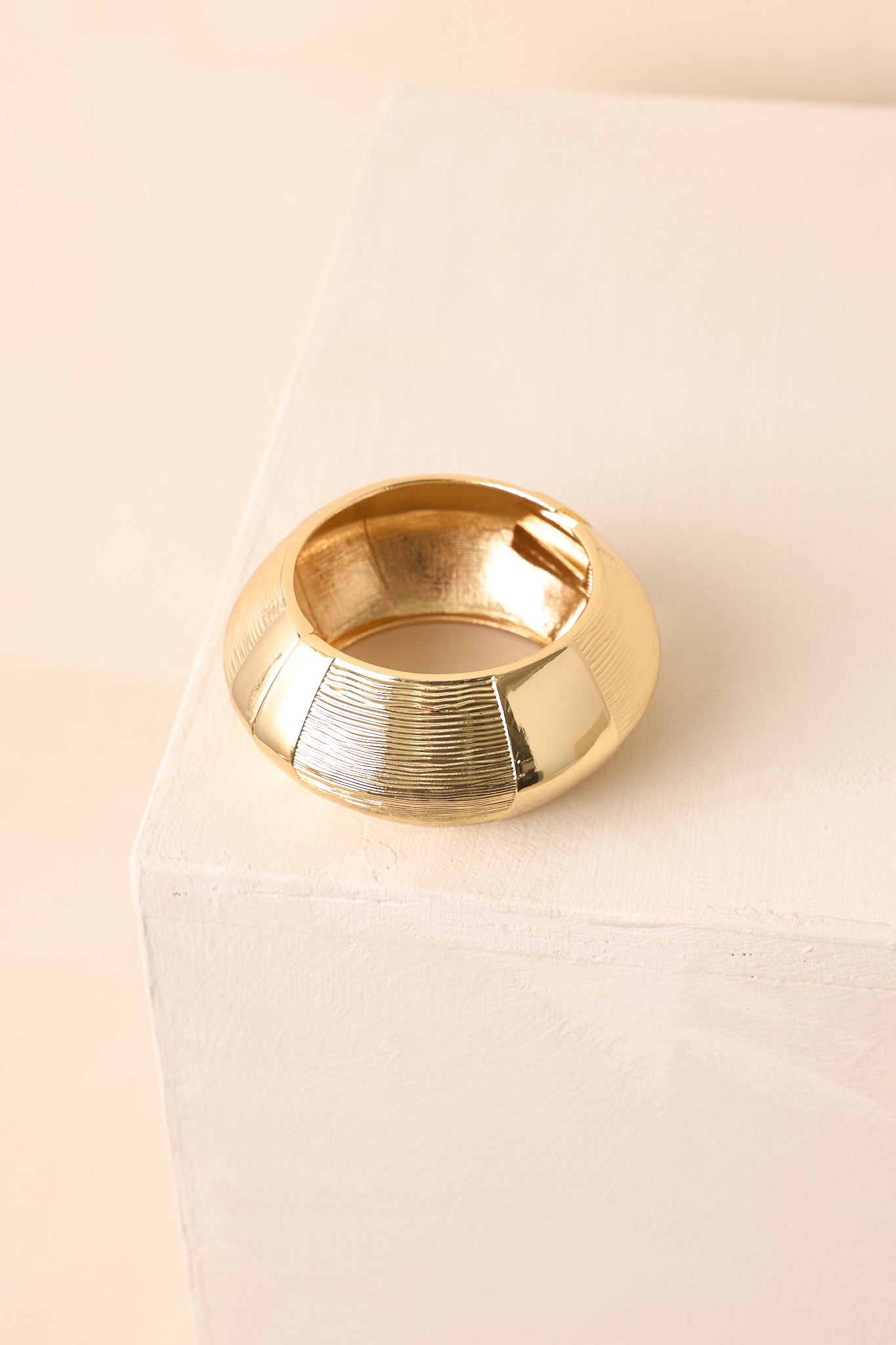 A detailed shot of the gold cuff bracelet focusing on engraved linear texture and glossy metal sections.