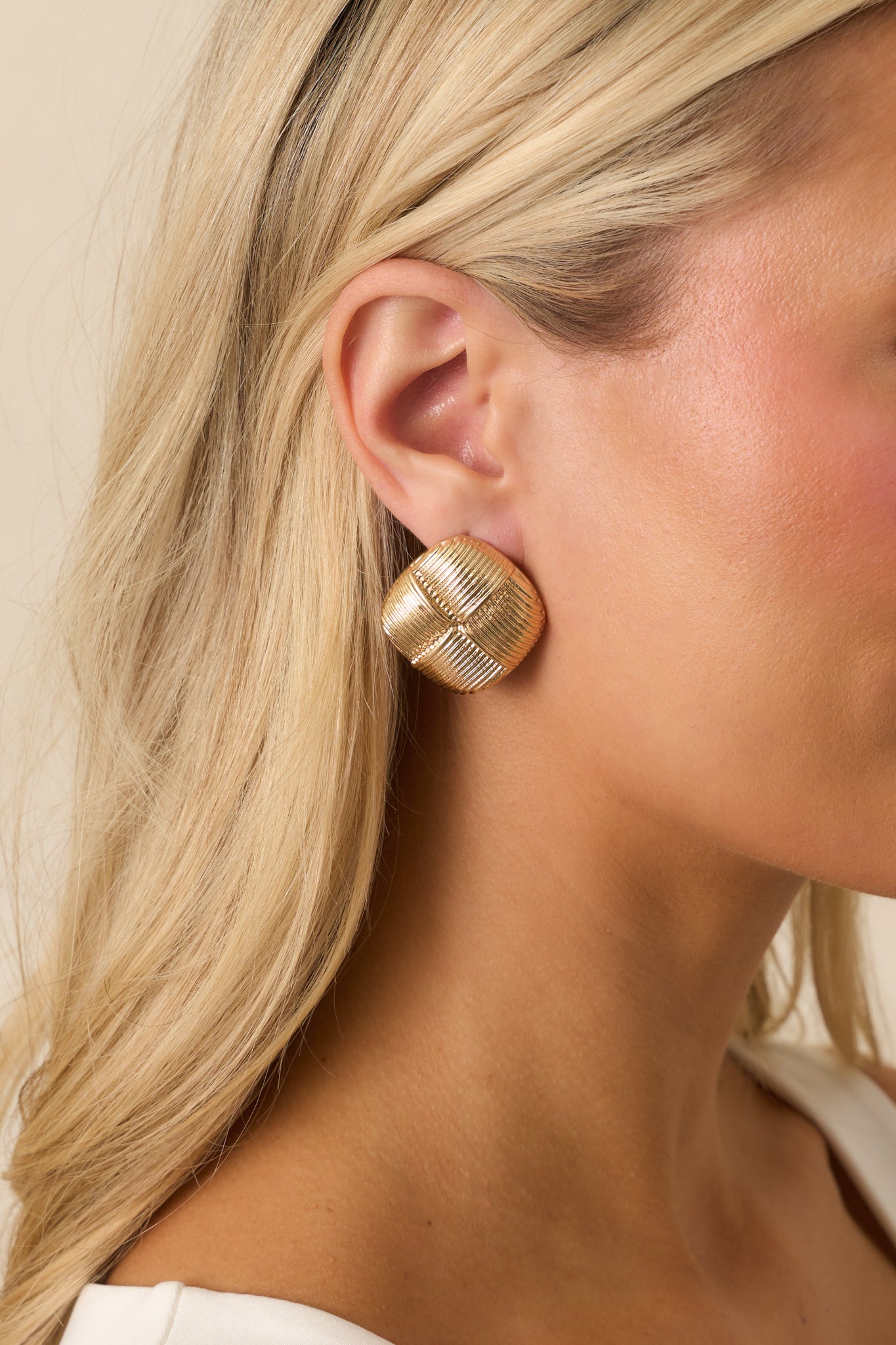 Cropped image showing gold square earrings with quadrant detailing and slightly raised domed surface.