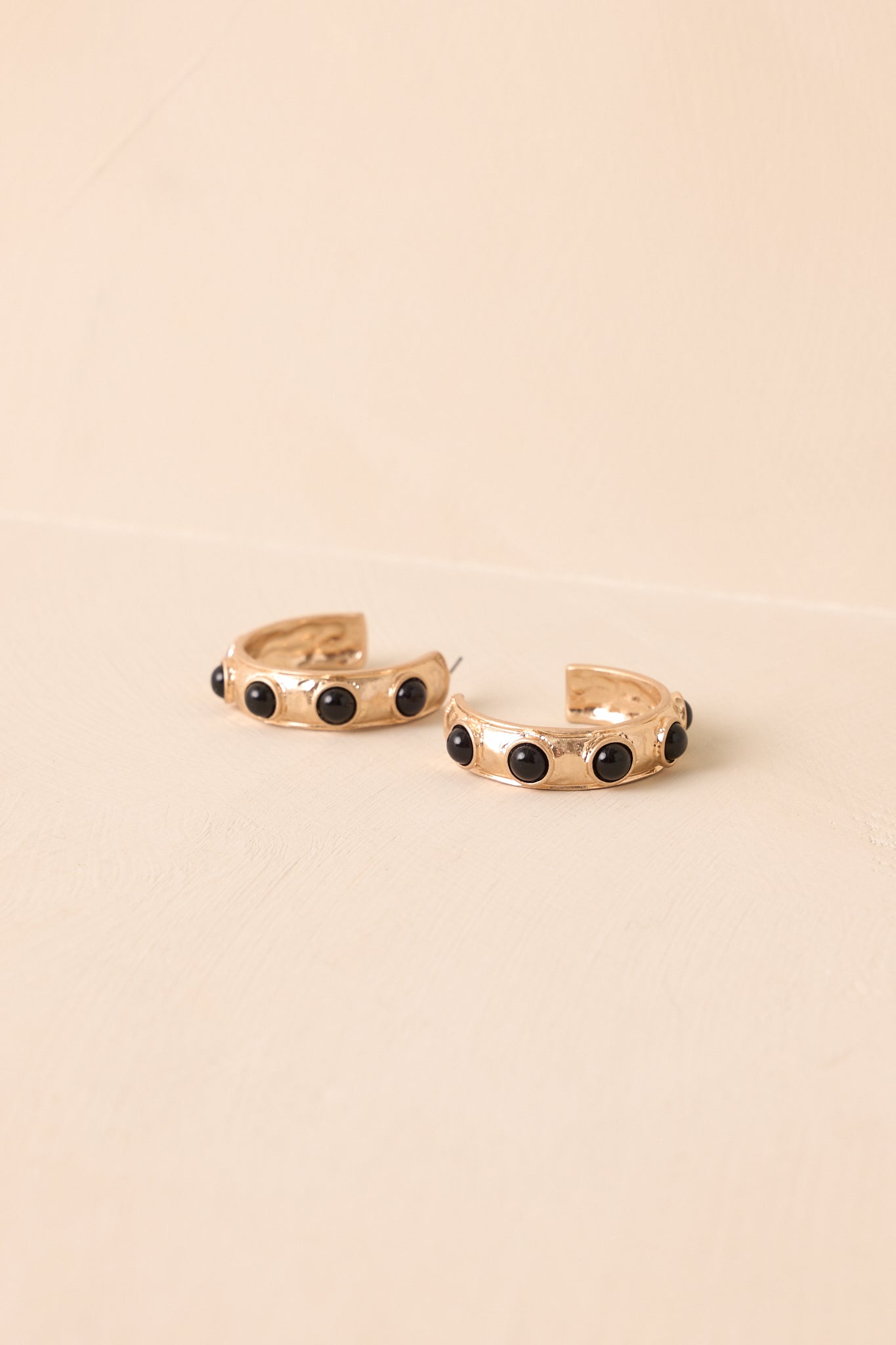 Gold hoop earrings with evenly placed circular black stones in a flat lay front view.