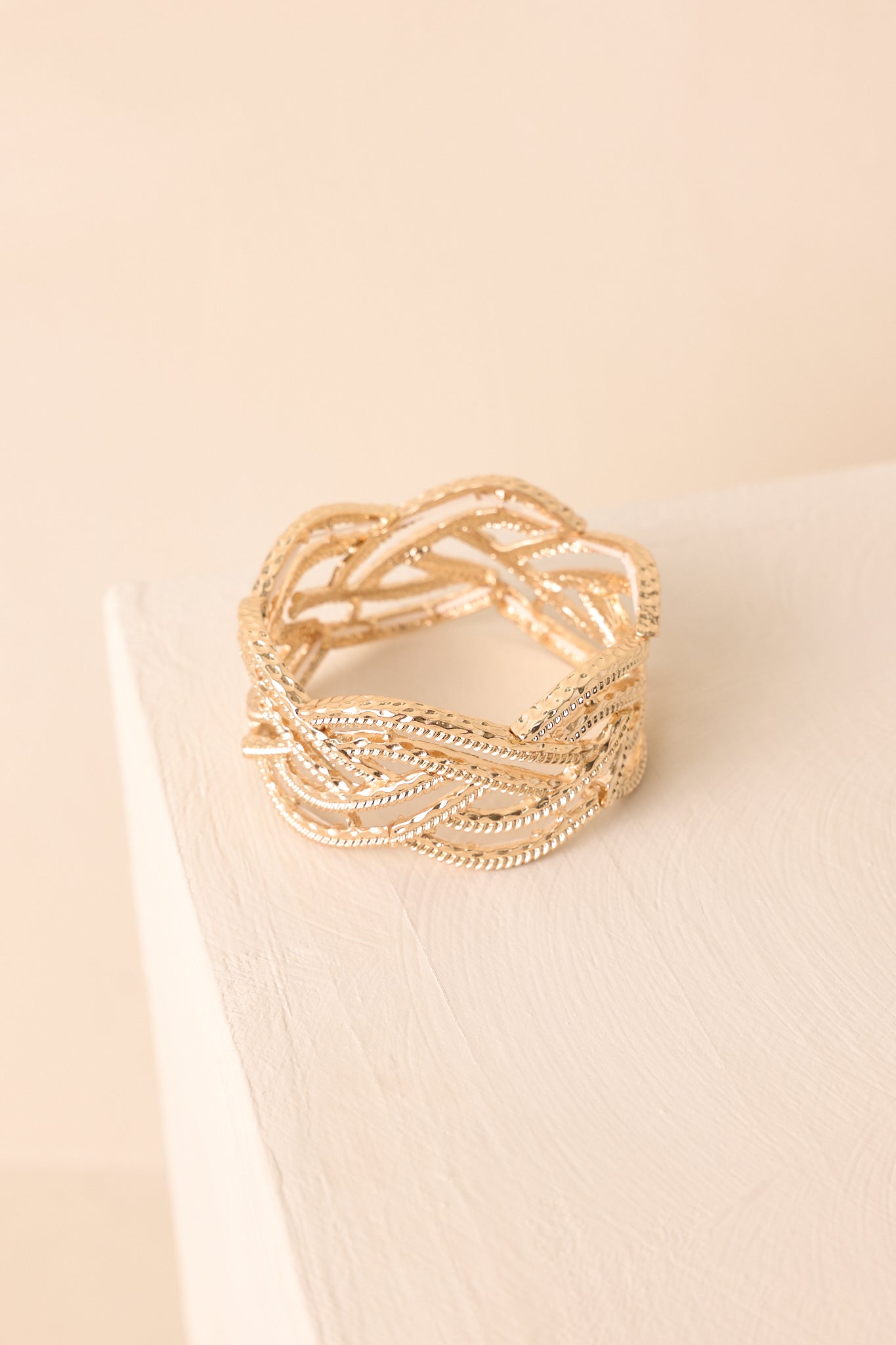 A zoomed-in overhead shot of the gold open braided bracelet with diamond-cut texture displayed against a beige background.