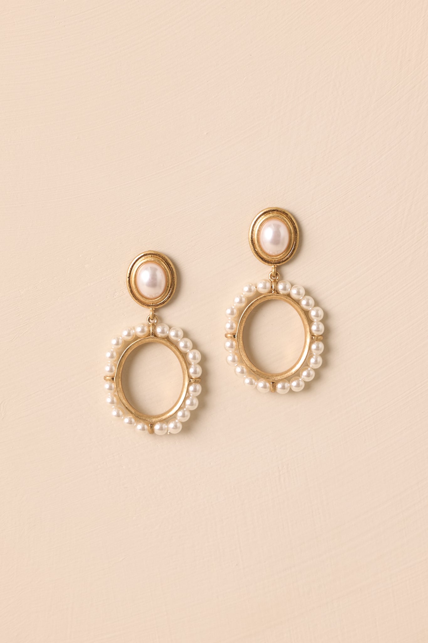 Flat lay of gold oval stud earrings with ivory pearl center and circular pearl drop charm.