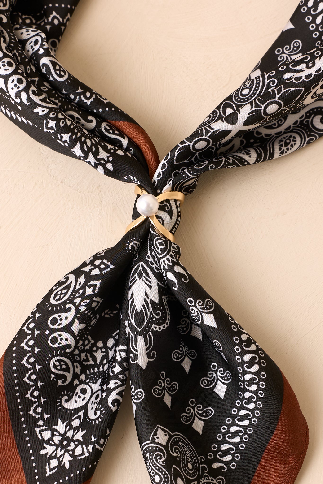 Close-up of a gold pearl scarf ring securing a black paisley scarf for a polished finishing touch.
