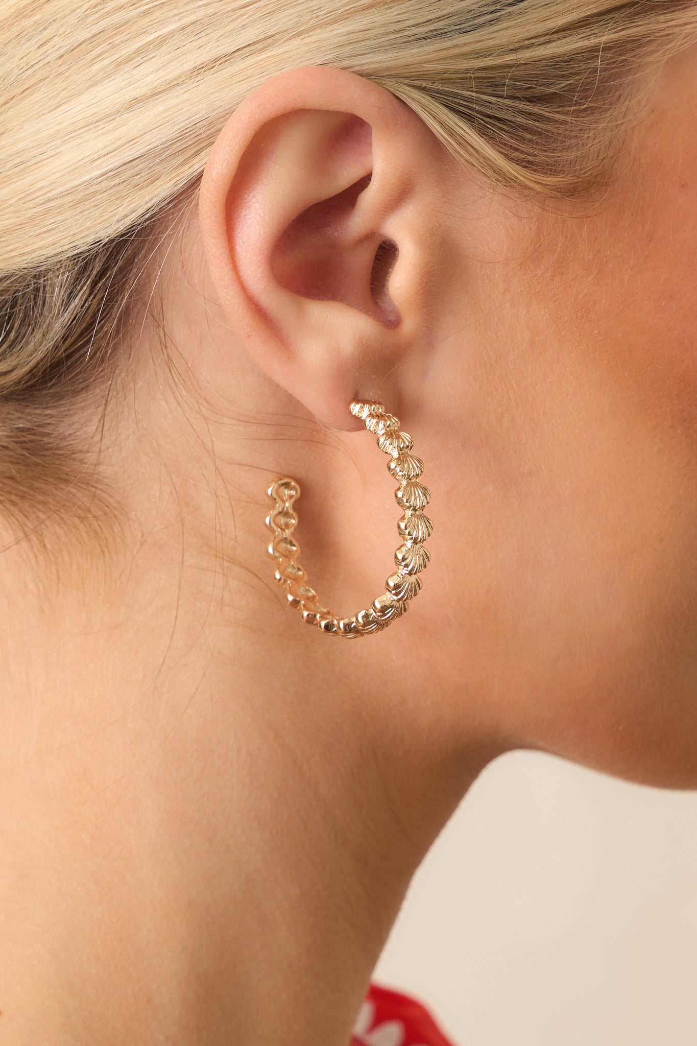 Closeup view of gold scalloped hoop earrings with seashell texture on model.