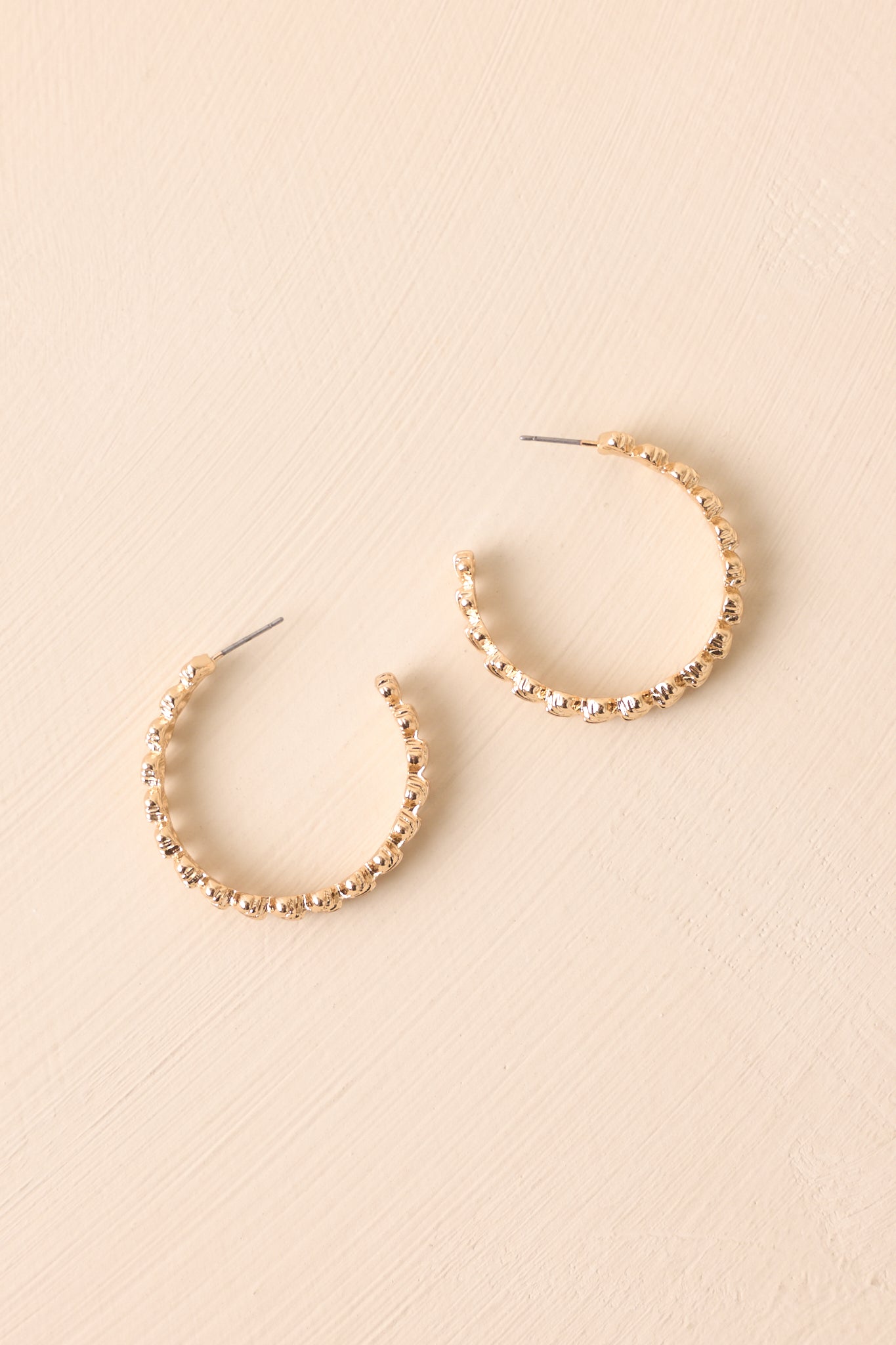 Flat lay of gold scalloped hoop earrings with seashell texture displayed on backdrop.