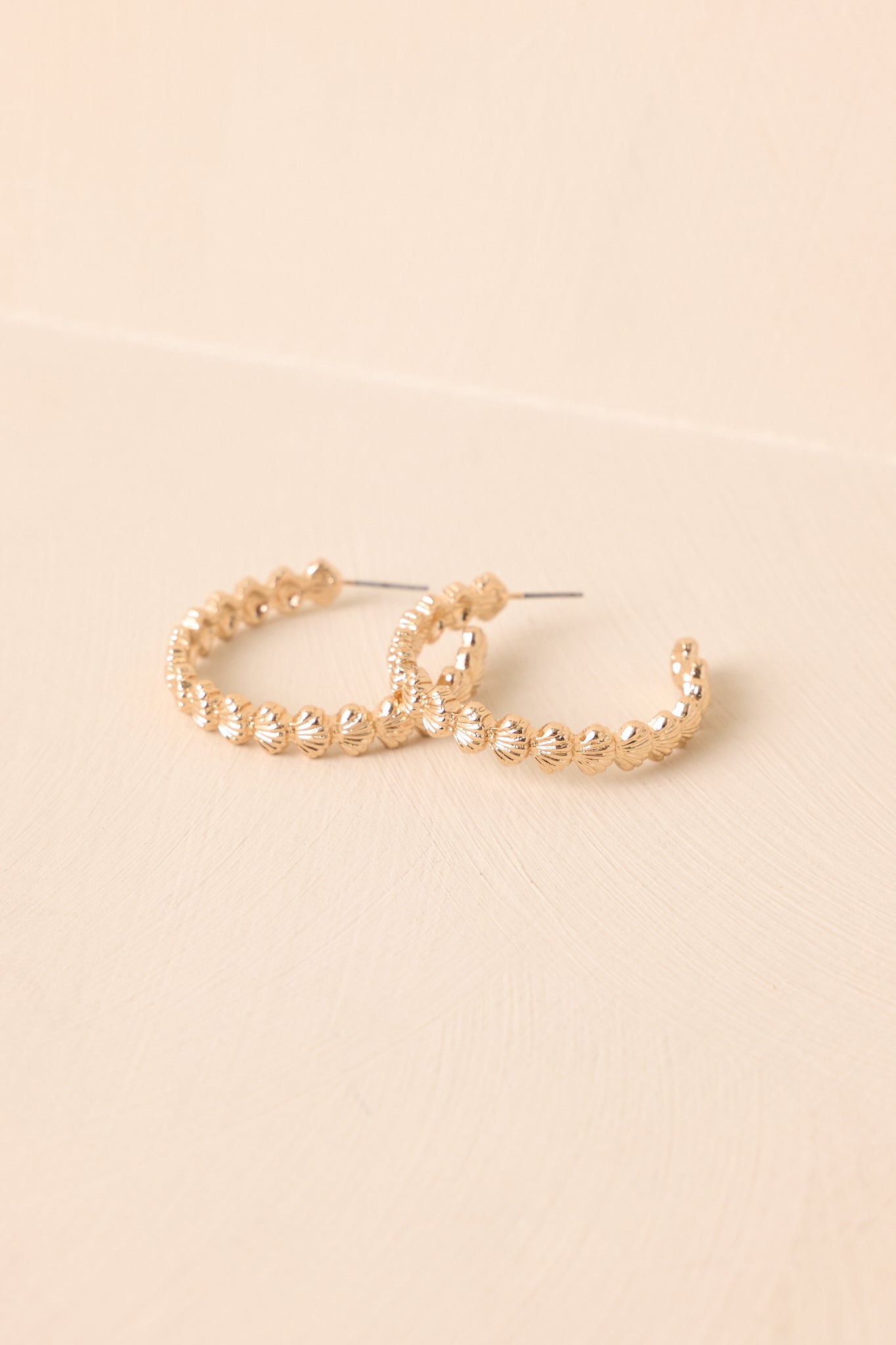 Pair of gold scalloped hoop earrings overlapped on neutral backdrop.