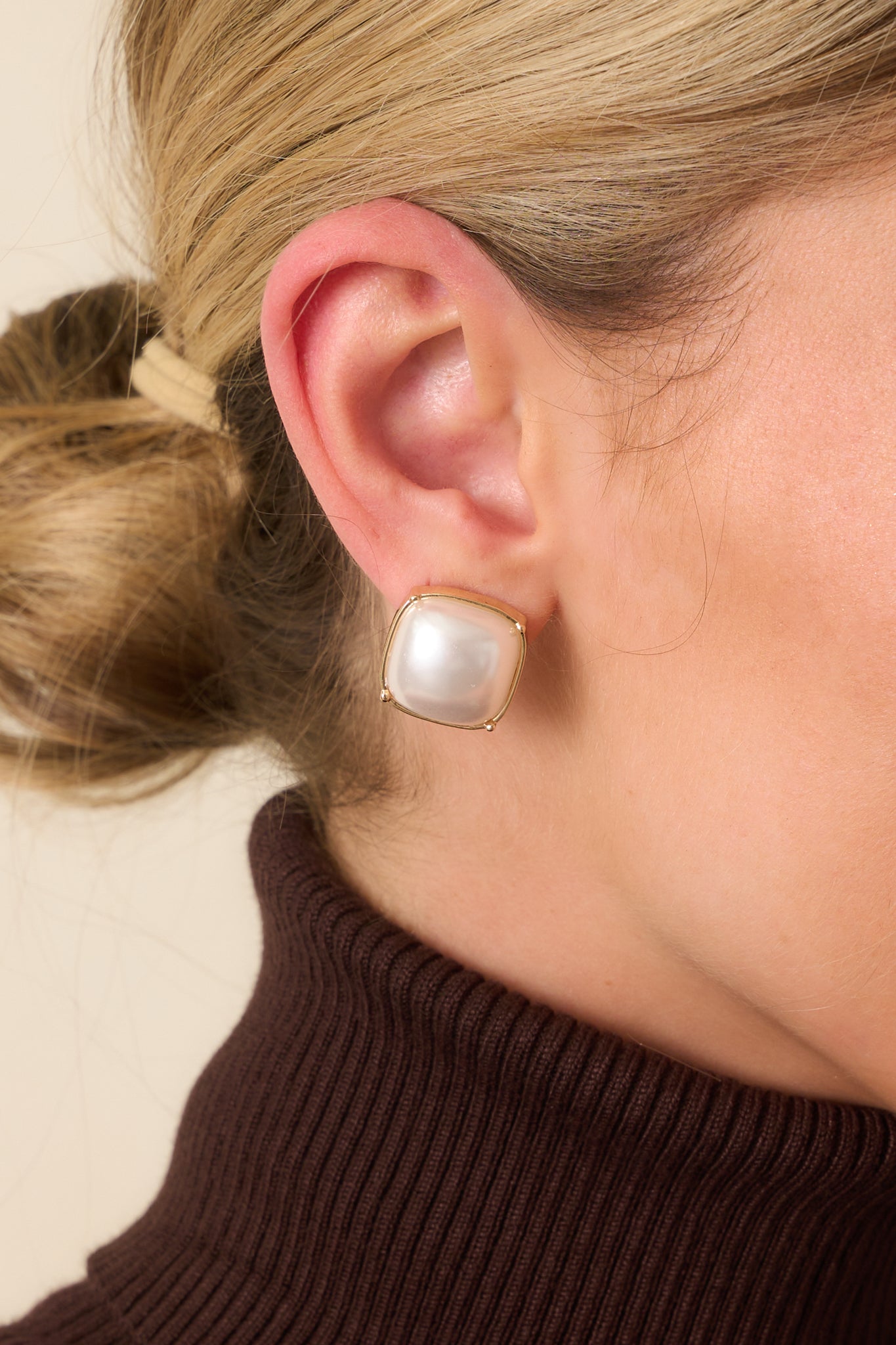 Cropped view of the earrings showing the square domed faux pearl center and rounded cushion-cut gold-tone setting