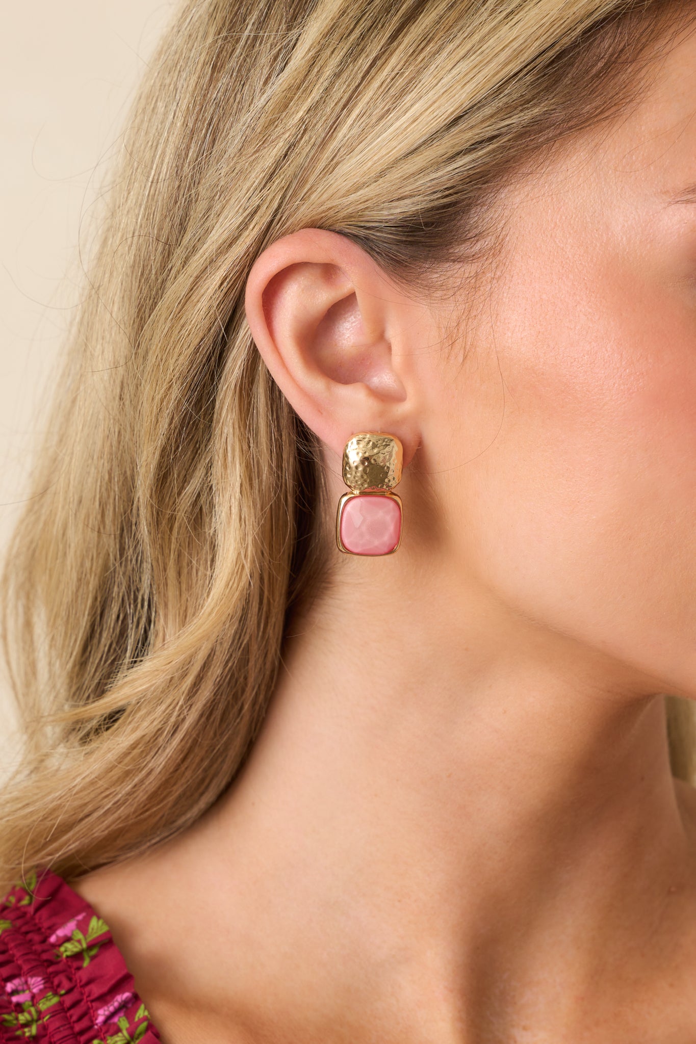 Cropped close-up of one earring displaying the textured gold stud and vibrant pink bezel-set gemstone.