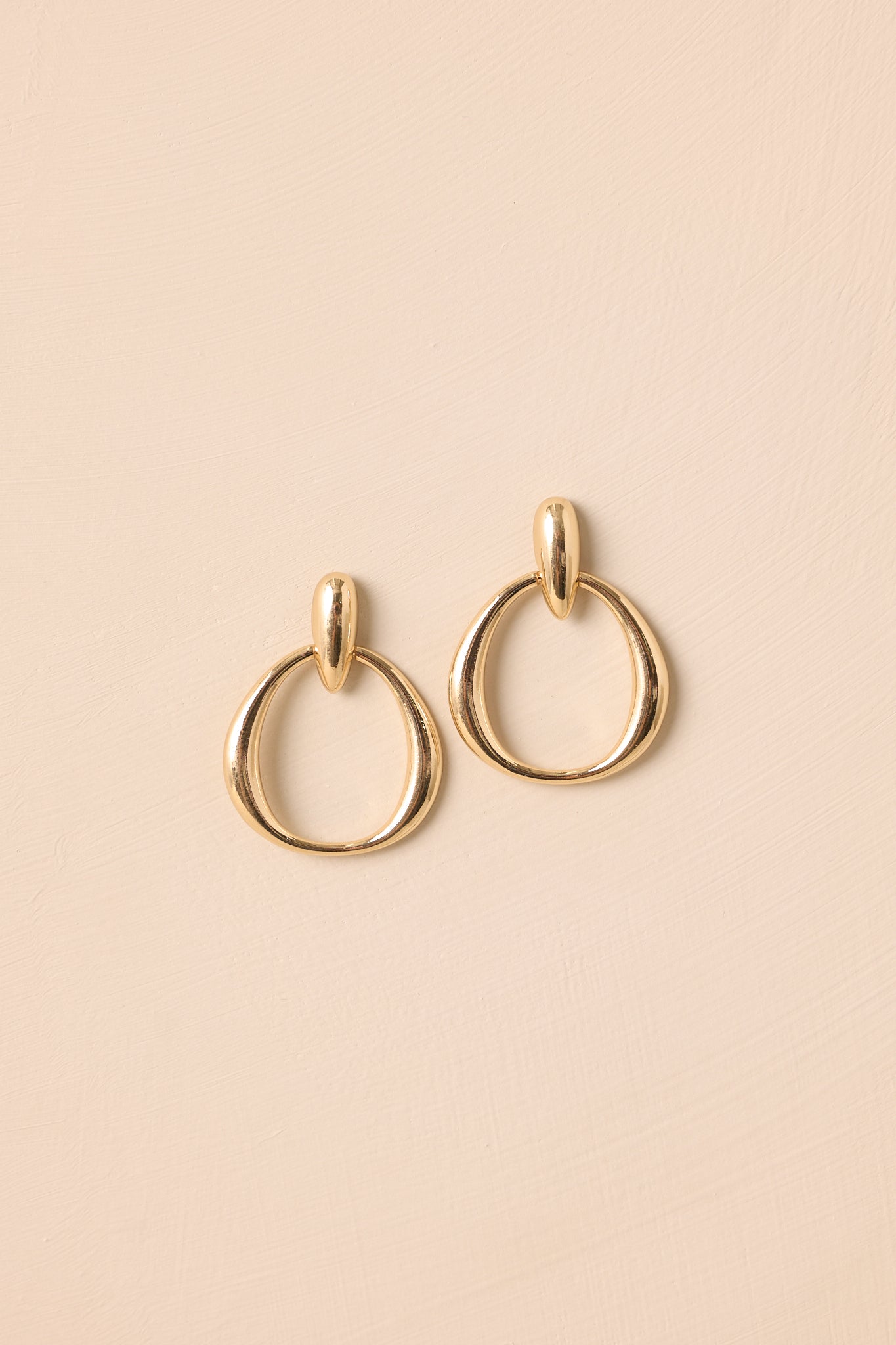 Flat lay of gold teardrop stud earrings with circular drop link.