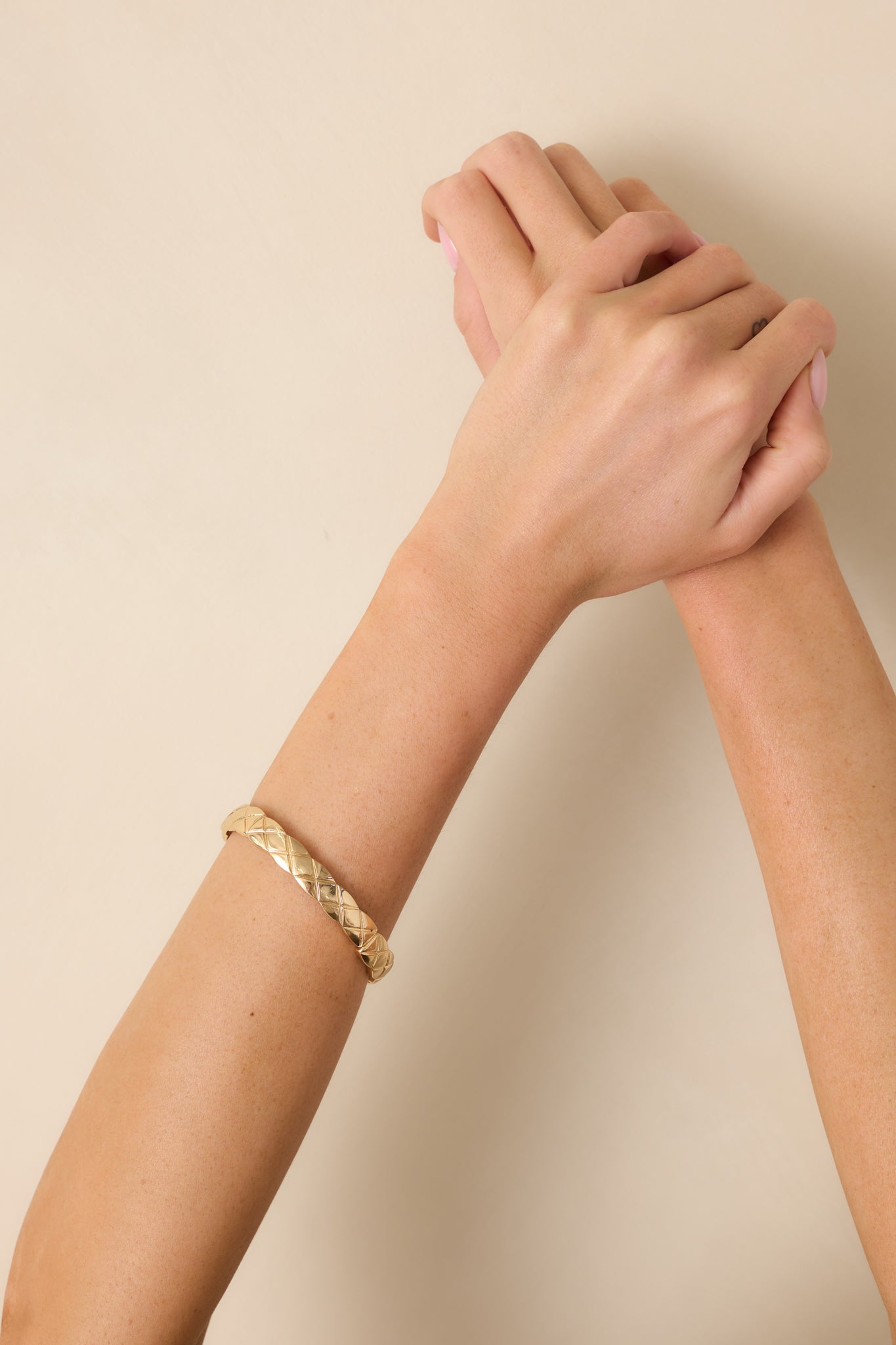 Cropped view of the gold-tone bangle bracelet showing the embossed crisscross pattern.