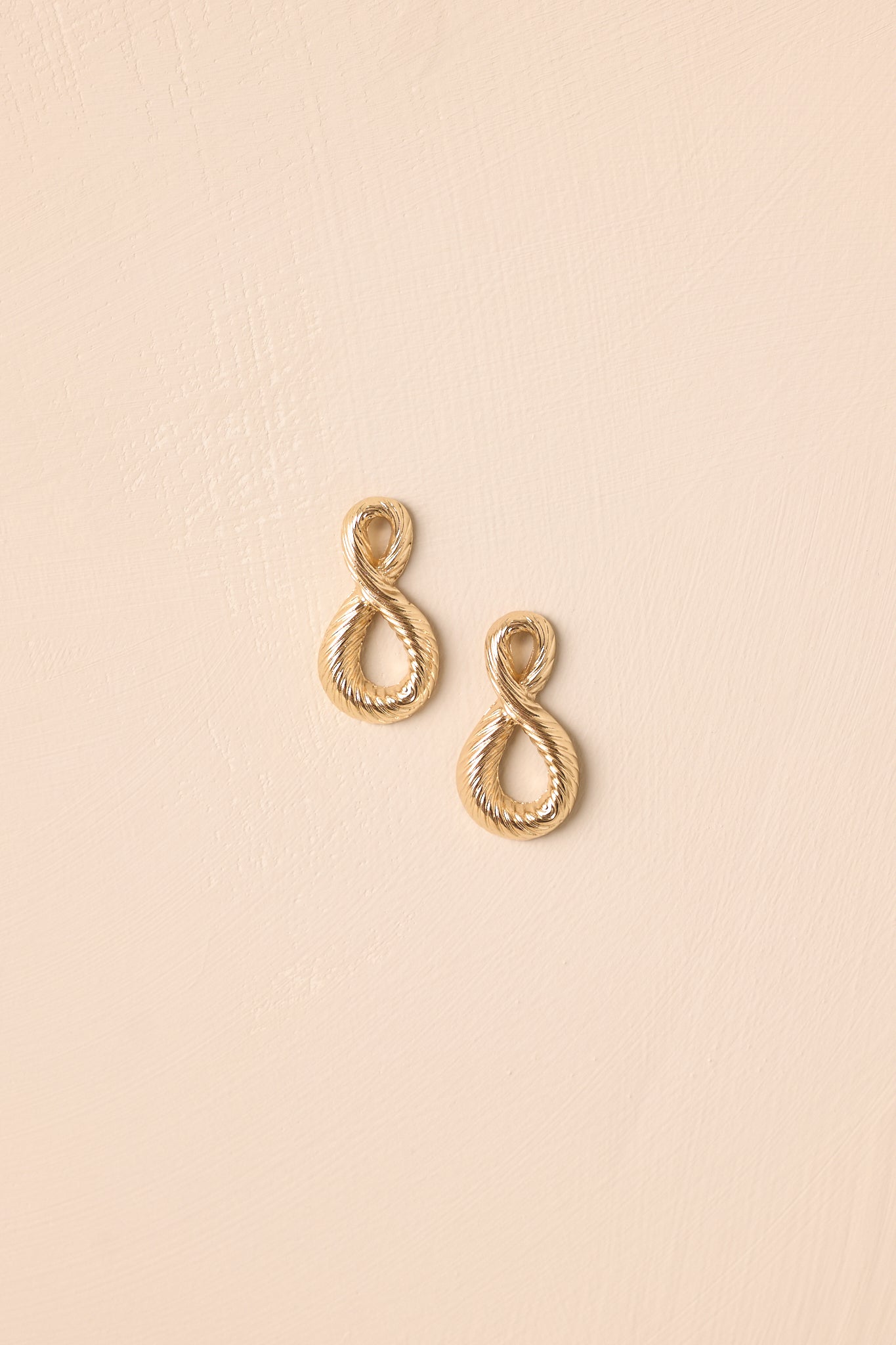Front view of the gold-tone earrings highlighting the abstract teardrop silhouette and twisted rope design on beige background.