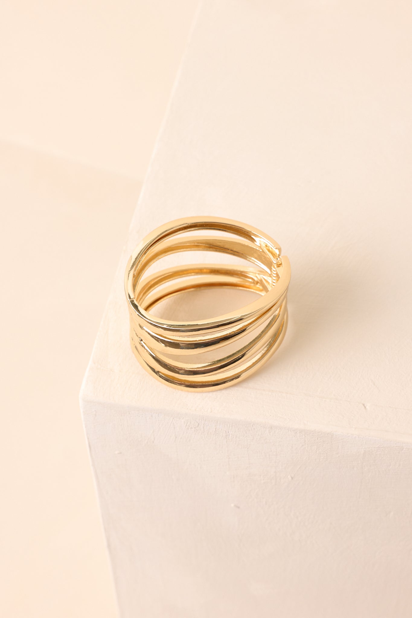 Gold cuff bracelet with three smooth, wide, flat metal bands and solid curved end caps, displayed on beige background.