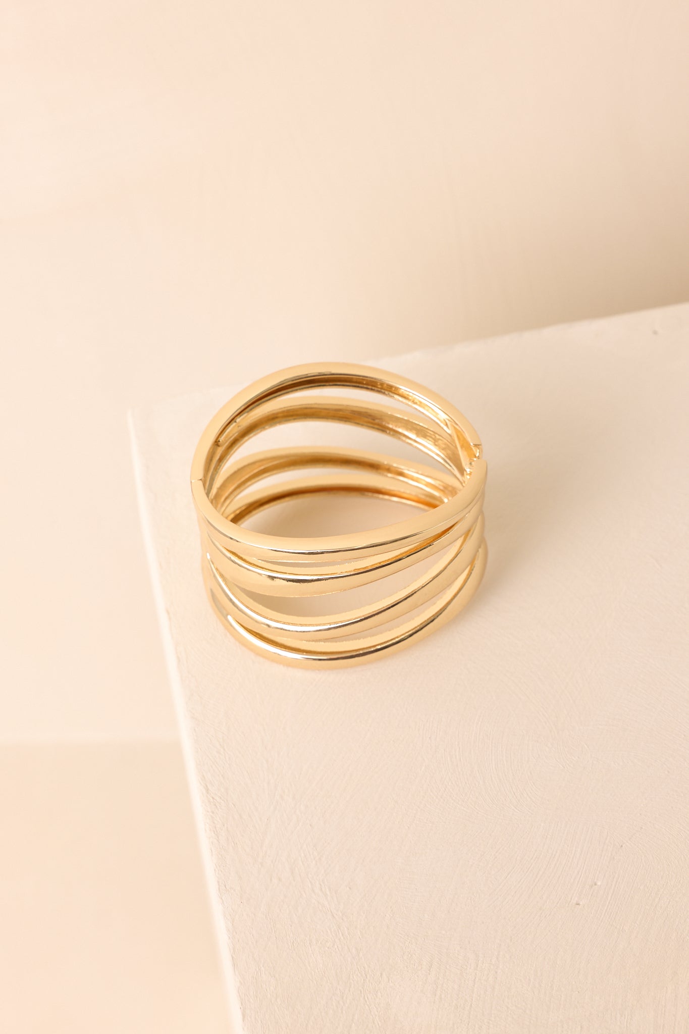 High-polish gold cuff bracelet showing evenly spaced convex bands and open design, set against beige backdrop.