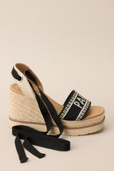 Close up side view of these black platform wedge sandals that feature a rounded toe, a strap over the top of the foot and around the heel, adjustable self-tie straps around the ankle, and a wedged heel.