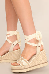 Close up Side view of these sandals that feature a rounded toe, a strap over the top of the foot and around the heel, adjustable self-tie straps around the ankle, and a wedged heel.