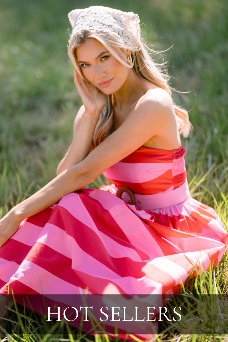Model sitting in grass wearing a pink striped summer dress and knit scarf on head. Dress is featured in our Hot Sellers Collection. 