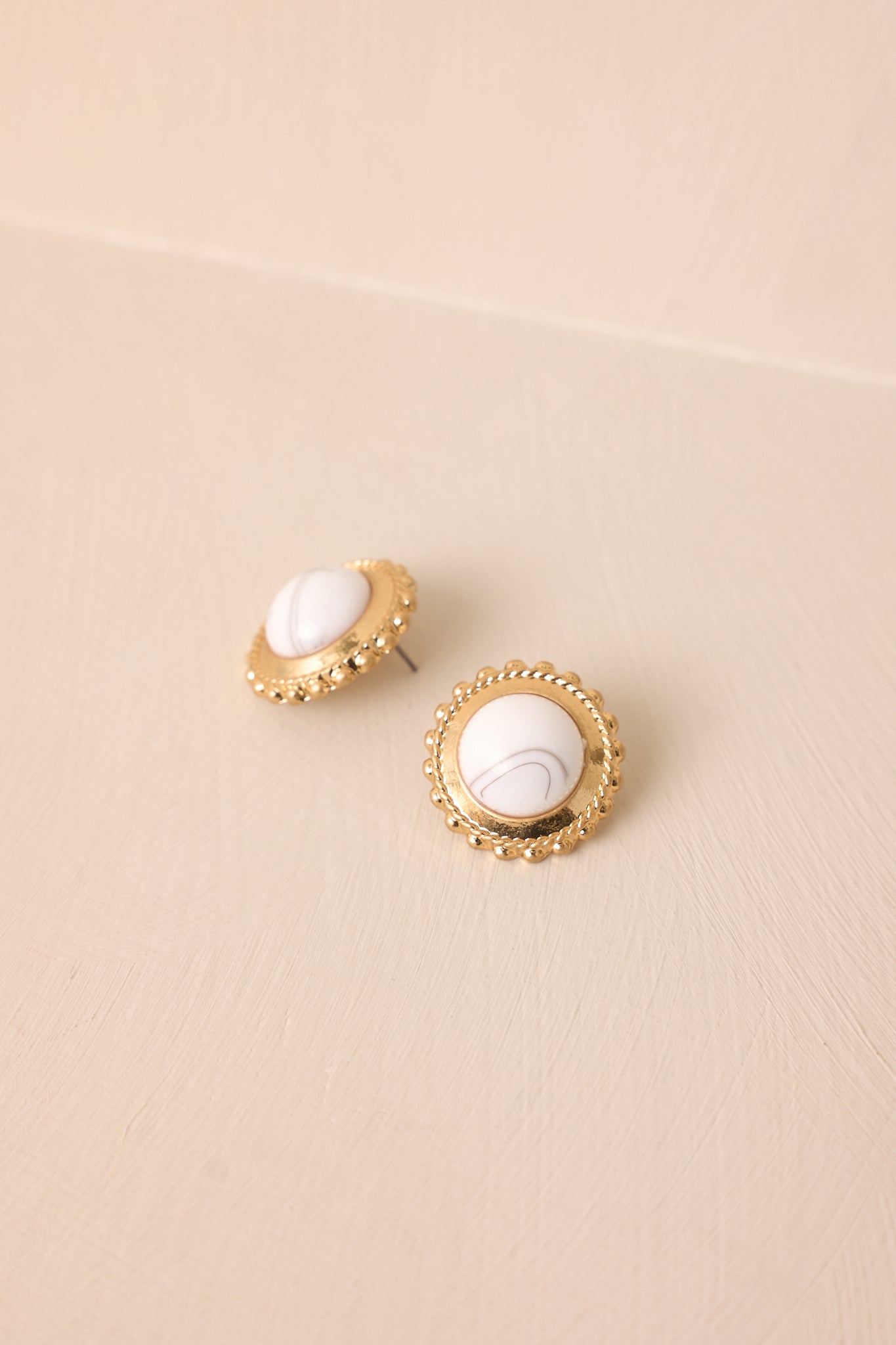 Angled flat lay of howlite and gold circular stud earrings highlighting circular shape, gold border, and textured beaded edge.
