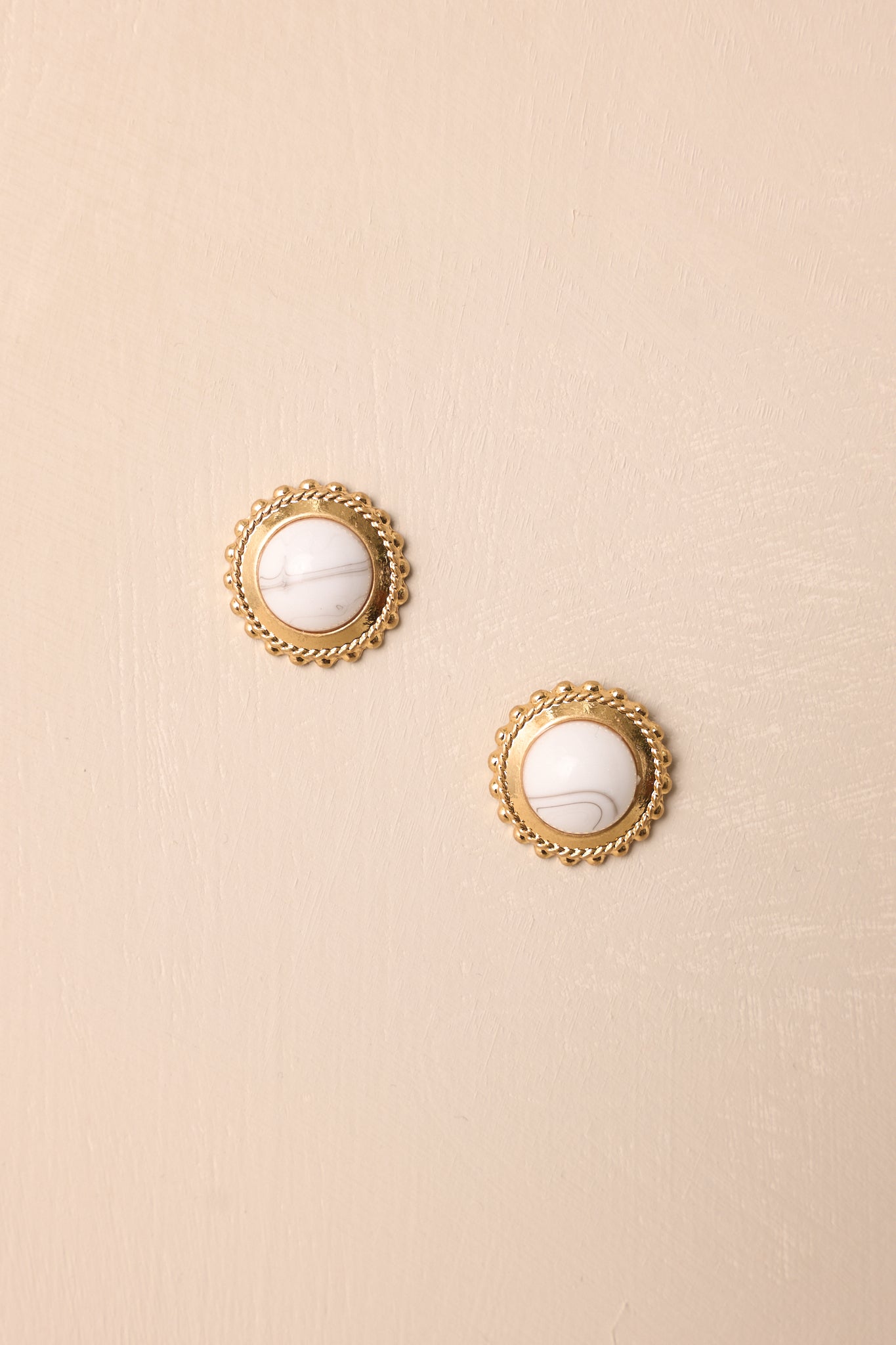 Flat lay of howlite and gold circular stud earrings showing large stone center with gold border and beaded detailing.
