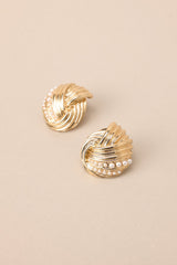 Close up view of these gold earrings with intertwined design and small faux pearl detailing, secure post backings.