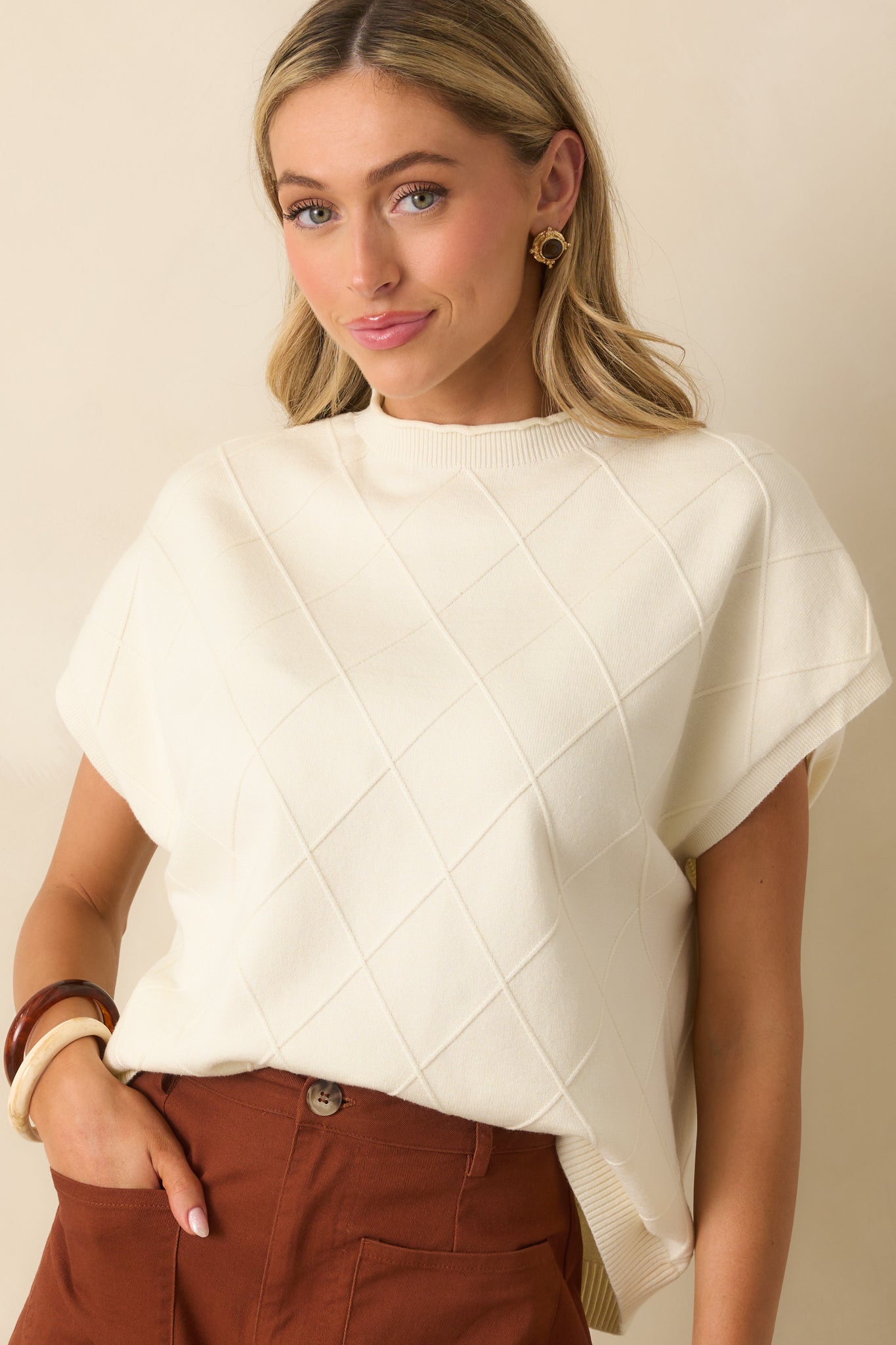 Up-close look at the argyle stitch design and rolled neckline of the ivory sweater.