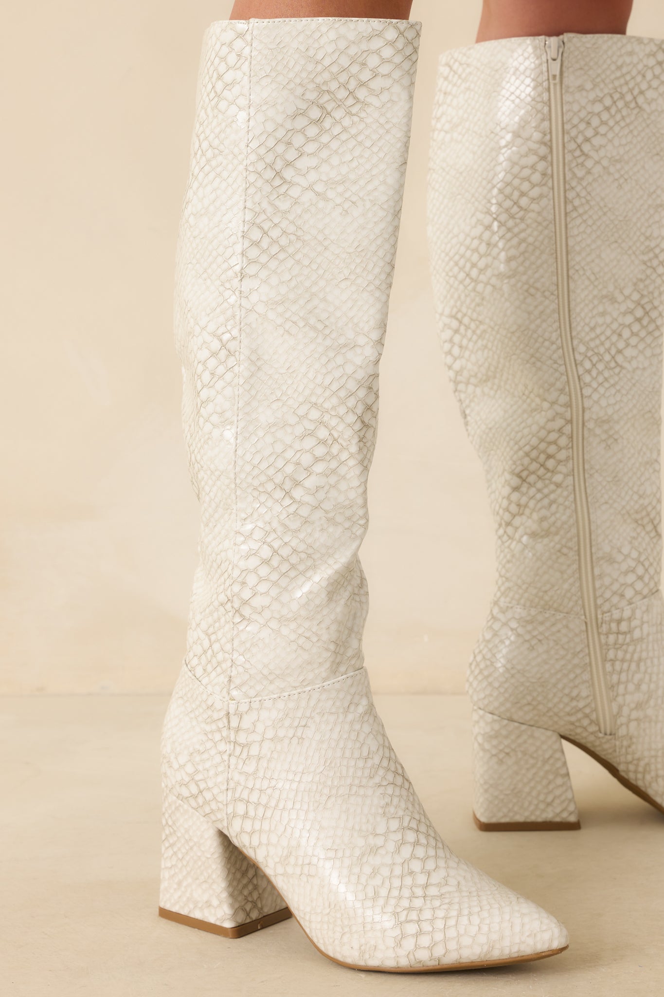 A cropped view of the ivory boots showing the pointed toe and textured snakeskin embossing.