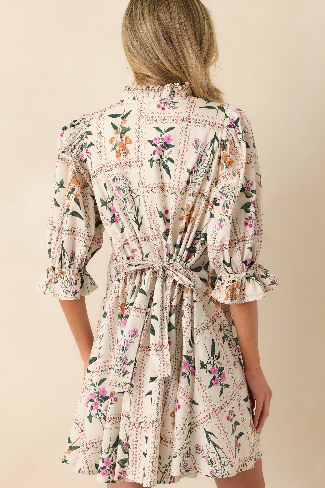 A back view of the ivory mini dress featuring the self-tie drawstring waist and continuation of the patchwork floral print.