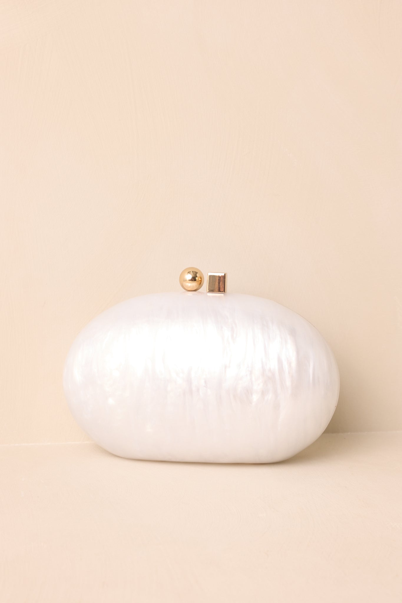 Close view of the ivory clutch highlighting its glossy finish and gold box clasp.