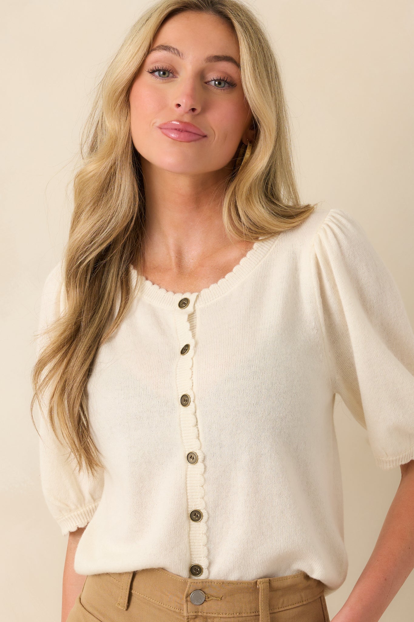 A cropped image showing the texture of the knit fabric and one of the short sleeves with scalloped edges.
