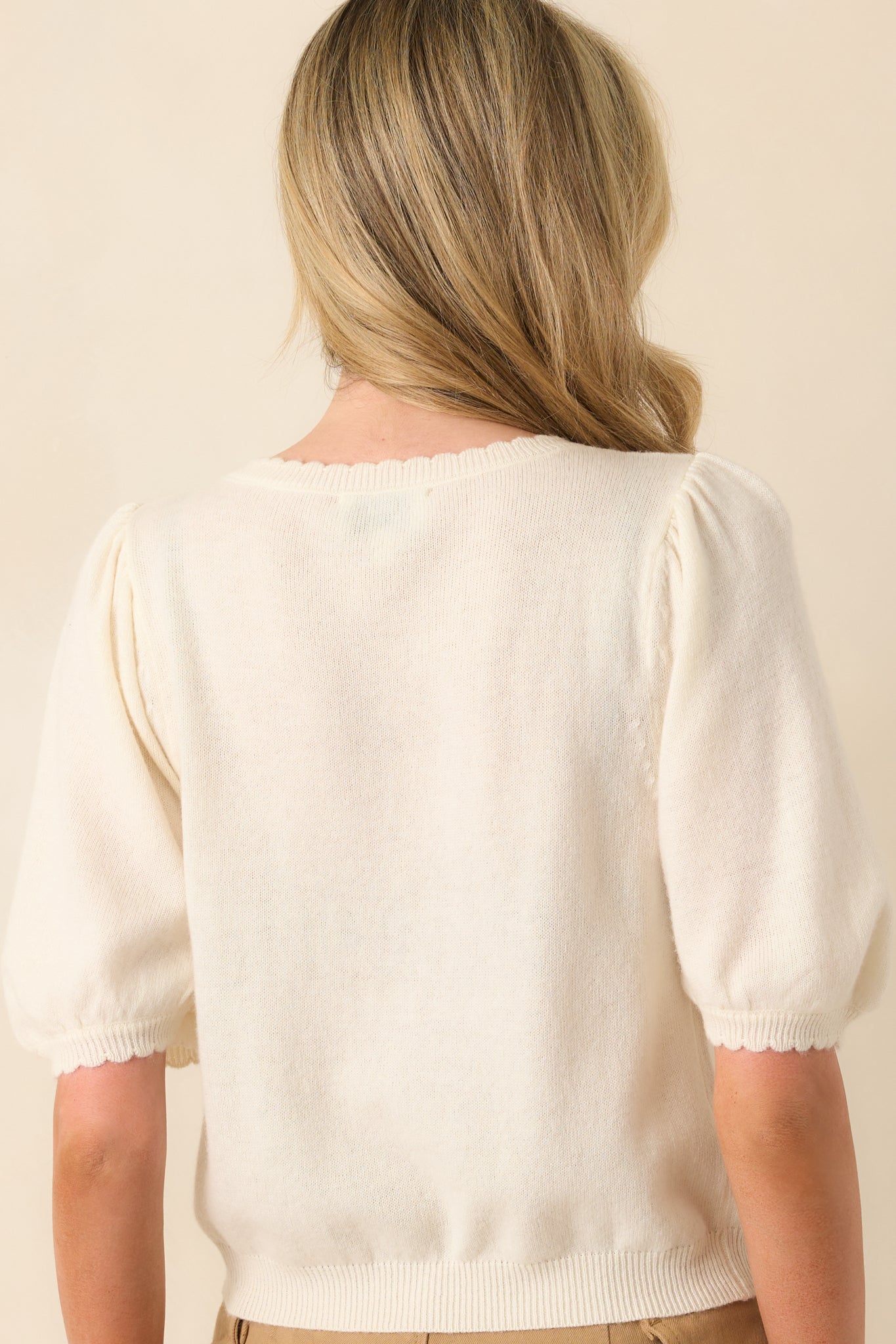A back view of the cardigan displaying the smooth knit fabric and short sleeves with scalloped edges.