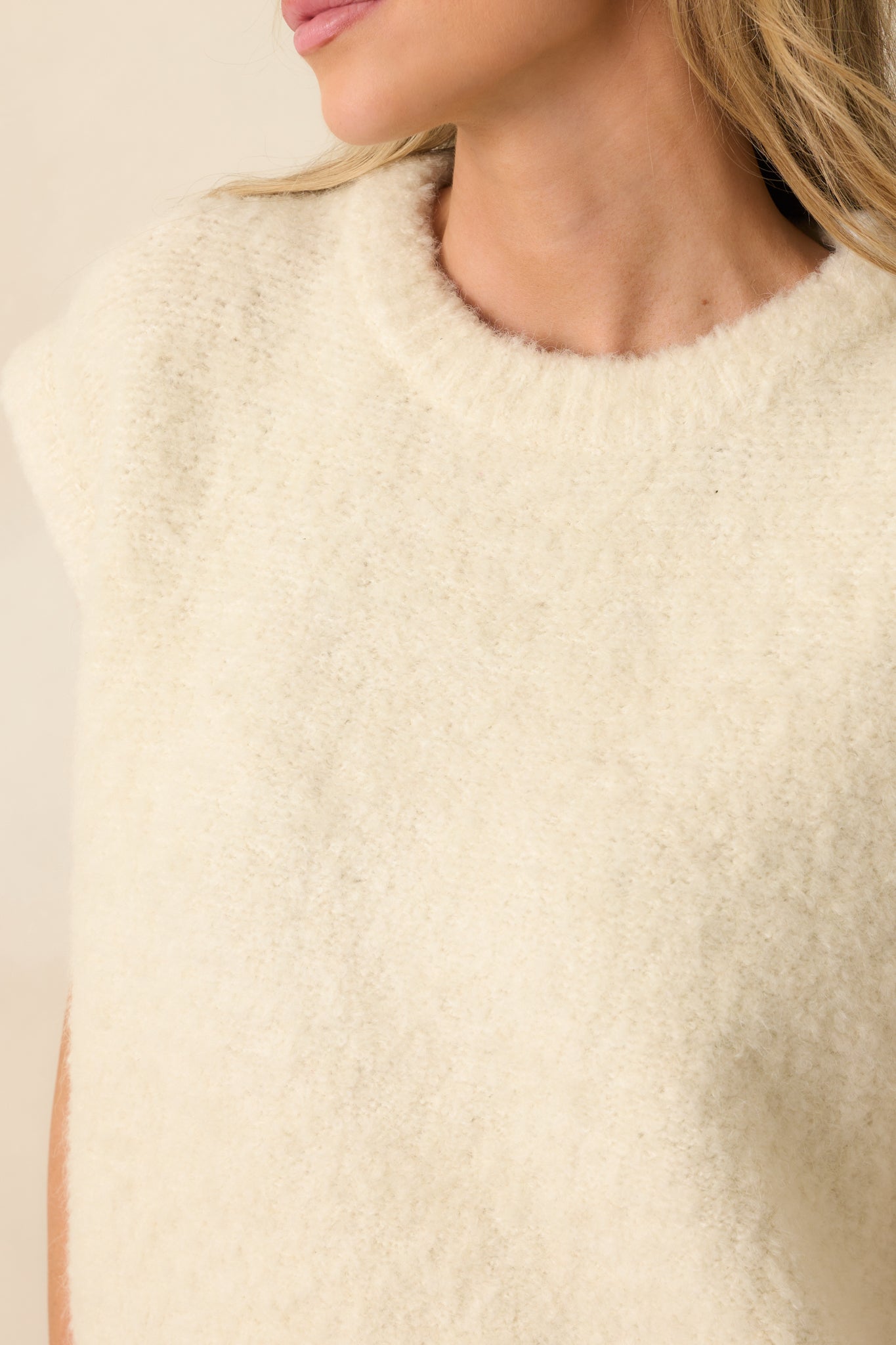 Fabric close-up displaying the soft knit texture and ivory color of the sweater vest.