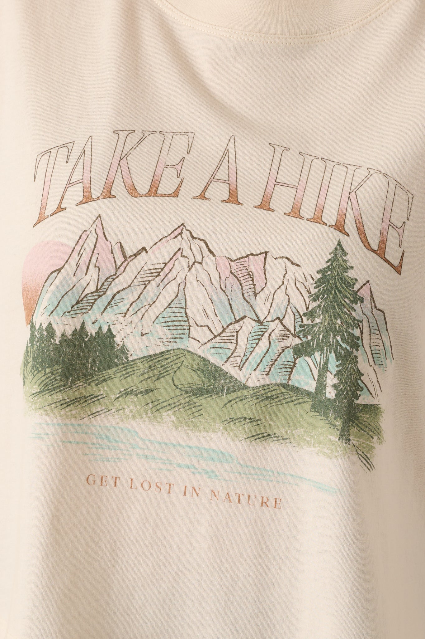 Close-up of “Take A Hike” mountain landscape front graphic on ivory tee.